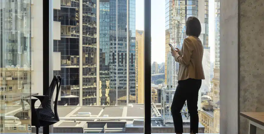 woman staring out city window with phone in hand