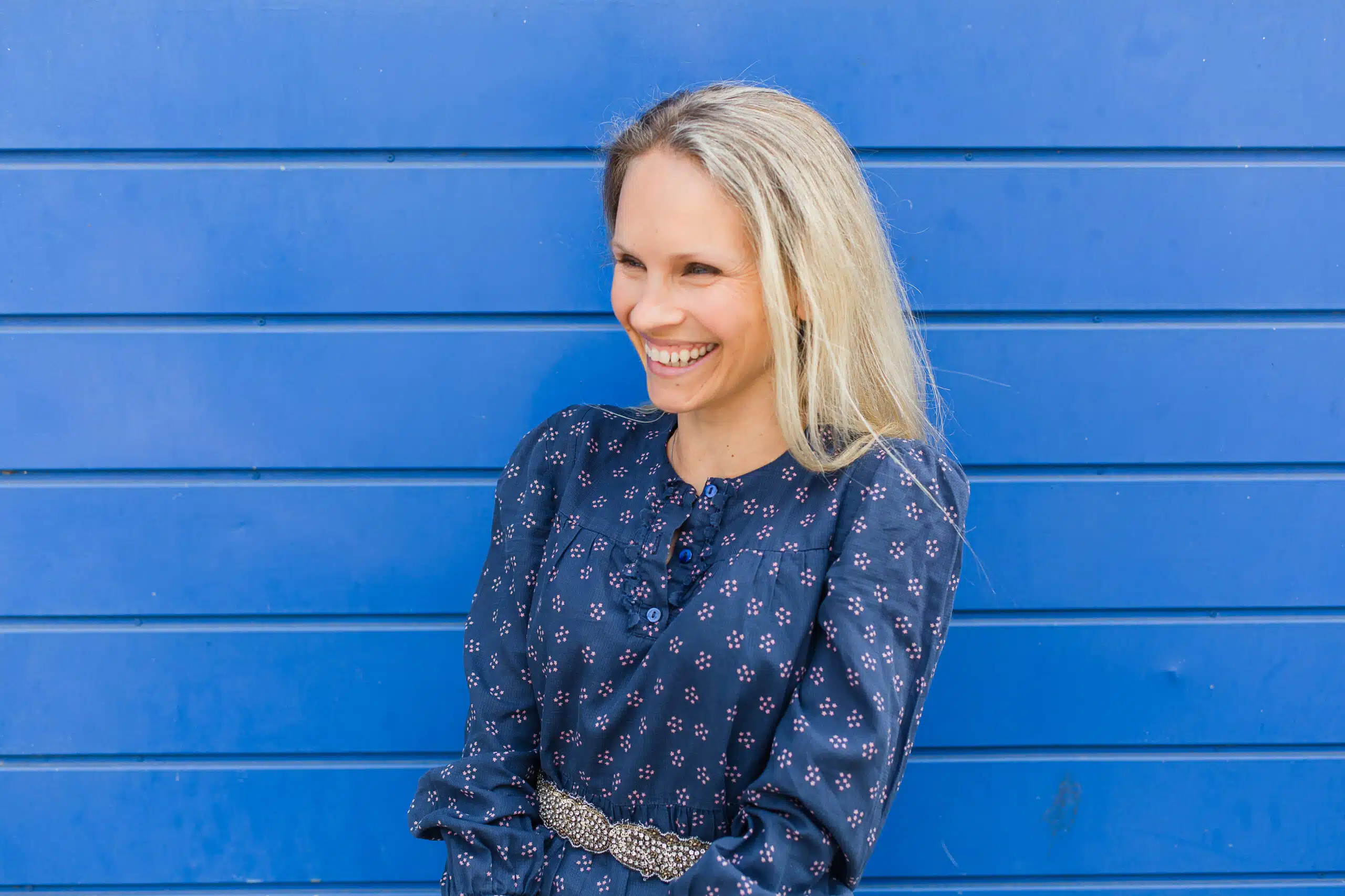 woman in dark blue dress smiling against a bright blue background