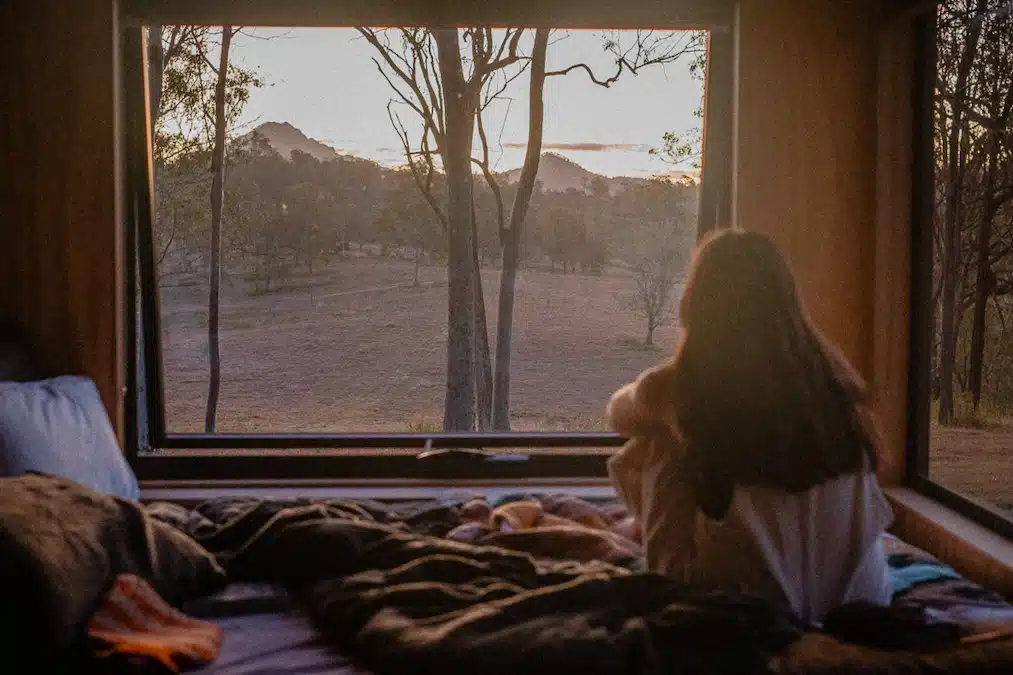 Girl resting in an Unyoked cabin, staring at nature scene outside